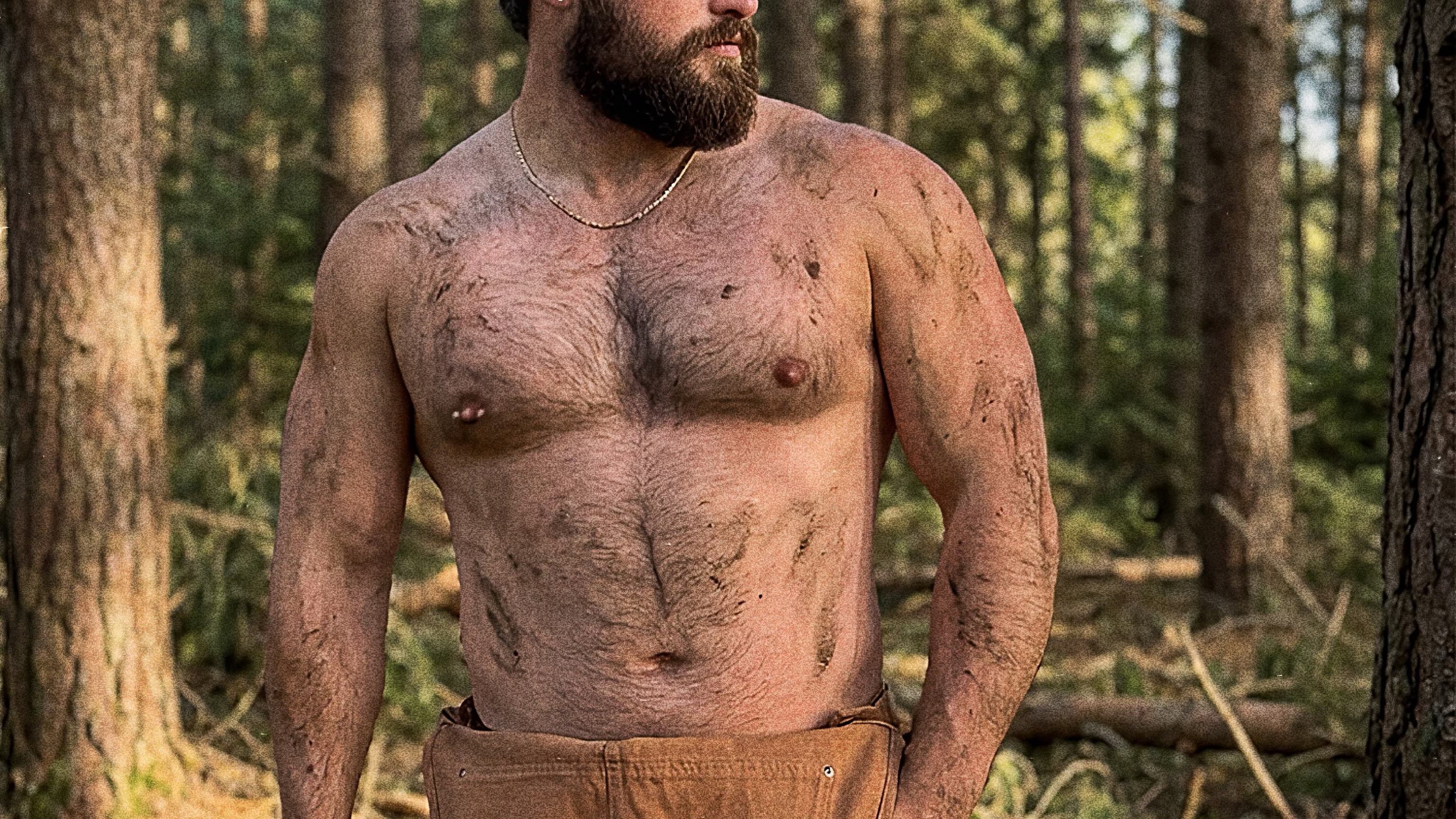 Man with a beard standing in a forest holding an axe.